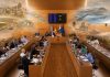 Pleno Tenerife mayo 2026: una isla entre gestión y relato Vista fotorrealista del salón de plenos del Cabildo de Tenerife, con los consejeros reunidos y, sobre la escena, imágenes difuminadas que evocan los grandes temas tratados: vivienda, movilidad, agua, energía, servicios sociales, sostenibilidad y protección del territorio.
