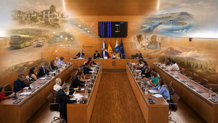 Vista fotorrealista del salón de plenos del Cabildo de Tenerife, con los consejeros reunidos y, sobre la escena, imágenes difuminadas que evocan los grandes temas tratados: vivienda, movilidad, agua, energía, servicios sociales, sostenibilidad y protección del territorio.