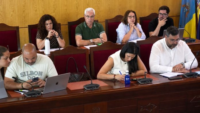 Pleno 1 Representantes municipales sentados en el salón de plenos del Ayuntamiento de Candelaria durante una sesión ordinaria, con documentación, micrófonos y ordenadores sobre la mesa.