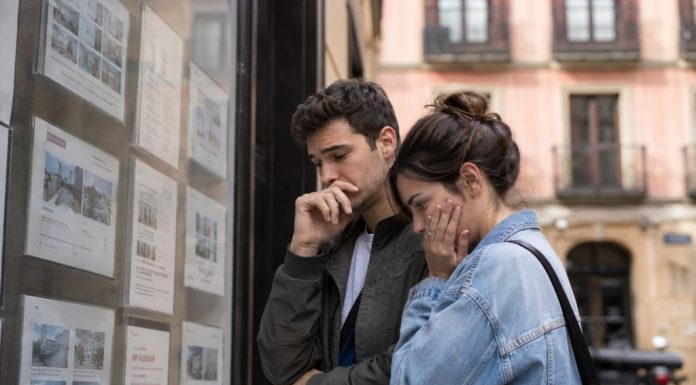 La crisis de vivienda ya rompe biografías Pareja joven observa con preocupación varios anuncios de alquiler en el escaparate de una inmobiliaria, reflejando la dificultad de acceder a una vivienda digna.