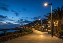 Alumbrado público de Candelaria: renovar con datos Paseo costero de Candelaria al anochecer, iluminado con luminarias LED de luz cálida junto al mar y con palmeras al fondo.