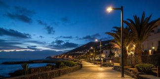 Alumbrado público de Candelaria: renovar con datos Paseo costero de Candelaria al anochecer, iluminado con luminarias LED de luz cálida junto al mar y con palmeras al fondo.
