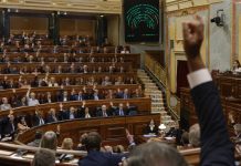 Bloqueo parlamentario: el coste para la ciudadanía Sesión de votación en el Congreso de los Diputados, con parlamentarios levantando la mano y el panel electrónico de resultados al fondo.