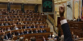 Bloqueo parlamentario: el coste para la ciudadanía Sesión de votación en el Congreso de los Diputados, con parlamentarios levantando la mano y el panel electrónico de resultados al fondo.