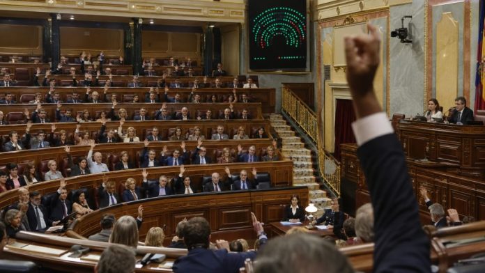 Sesión de votación en el Congreso de los Diputados, con parlamentarios levantando la mano y el panel electrónico de resultados al fondo.