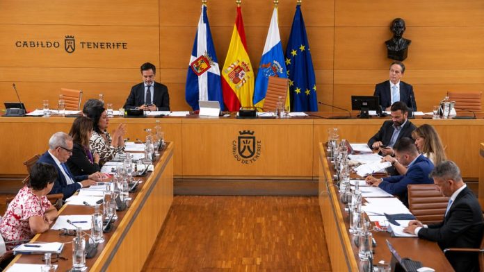 Sesión plenaria del Cabildo de Tenerife en su salón institucional, con representantes en las mesas de debate, presidencia, banderas oficiales y documentación de trabajo.