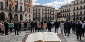 Laicidad pendiente: cuando se confunde respeto con pleitesía Constitución Española abierta en primer plano ante una ceremonia cívico-religiosa en una plaza institucional, como símbolo del debate sobre la laicidad pendiente y la neutralidad del Estado.