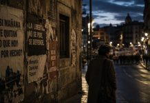 Miedo democrático: cuando la libertad vuelve a parecer vulnerable Persona caminando de noche por una calle urbana en penumbra, junto a carteles sobre libertad, memoria y derechos, como símbolo del miedo democrático ante la pérdida de libertades.