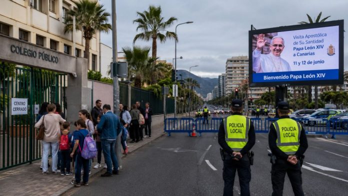 Papa 1 Familias ante un colegio público cerrado mientras la policía regula el tráfico en una avenida canaria con motivo de la visita del Papa.