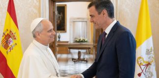 Papa y Sánchez: una sintonía que incomoda El papa León XIV y Pedro Sánchez se saludan cordialmente en una sala institucional, con las banderas de España y la Santa Sede al fondo, en una escena que representa diálogo diplomático y buena sintonía.