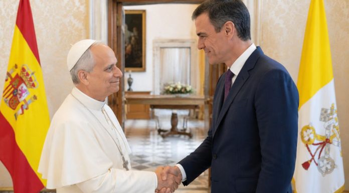 Papa y Sánchez: una sintonía que incomoda El papa León XIV y Pedro Sánchez se saludan cordialmente en una sala institucional, con las banderas de España y la Santa Sede al fondo, en una escena que representa diálogo diplomático y buena sintonía.