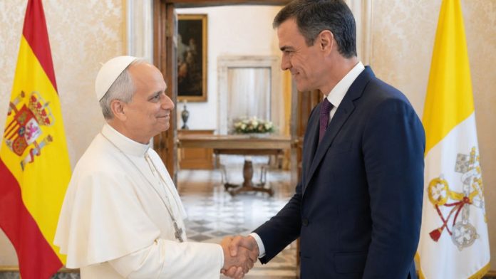 Papa 3 El papa León XIV y Pedro Sánchez se saludan cordialmente en una sala institucional, con las banderas de España y la Santa Sede al fondo, en una escena que representa diálogo diplomático y buena sintonía.