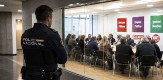Sindicatos de clase y Policía Nacional: derechos con uniforme Policía nacional observa desde un pasillo acristalado una reunión sindical, simbolizando el debate sobre su acceso a los sindicatos de clase.
