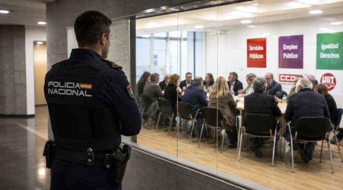 Sindicatos de clase y Policía Nacional: derechos con uniforme Policía nacional observa desde un pasillo acristalado una reunión sindical, simbolizando el debate sobre su acceso a los sindicatos de clase.