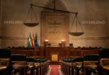 Pacto PP Vox Andalucía: derechos en retirada Interior vacío del Parlamento de Andalucía, con una gran balanza proyectada sobre el hemiciclo y las palabras “Derechos” y “Estabilidad” a ambos lados.