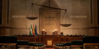 Pacto PP Vox Andalucía: derechos en retirada Interior vacío del Parlamento de Andalucía, con una gran balanza proyectada sobre el hemiciclo y las palabras “Derechos” y “Estabilidad” a ambos lados.