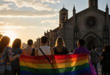 Declaraciones de Argüello: el Orgullo LGTBI+ no es pecado Grupo diverso de personas camina con una bandera arcoíris frente a una iglesia al atardecer, como símbolo del contraste entre condena religiosa y dignidad LGTBI+.