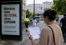 CEOE y bajas laborales: una campaña contra el enfermo Mujer con un parte de incapacidad temporal frente a una marquesina sobre el absentismo laboral, con un hospital y varios trabajadores al fondo.