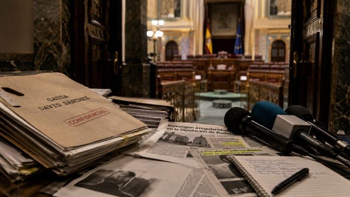 Expedientes judiciales, recortes de prensa y micrófonos ante una sala institucional, como símbolo de la tensión entre justicia, medios y confrontación política.