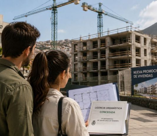 Licencias urbanísticas en Canarias: agilizar no basta Pareja observa una promoción de viviendas en construcción en Canarias mientras sostiene planos y una licencia urbanística, con un ayuntamiento y varias grúas al fondo.