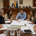 Oposición municipal: prepararse para gobernar Equipo plural de oposición analiza presupuestos, planos y proyectos municipales alrededor de una mesa situada frente al salón de plenos.