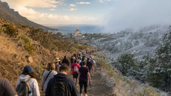 Peregrinos caminan hacia Candelaria por un sendero de Tenerife entre un paisaje seco de verano y otro más frío, simbolizando la adaptación de la tradición al cambio climático.