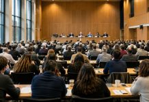 Ley de hierro: cómo el poder crea sus propias élites Asamblea democrática en un gran auditorio, con numerosos participantes frente a una pequeña mesa de dirigentes que concentra la atención y la toma de decisiones.