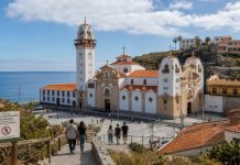 Afluencia en Candelaria: por qué hubo menos peregrinos Vista de la Basílica de Candelaria y su entorno costero con peregrinos descendiendo hacia la plaza y un aviso de restricción de sendero por riesgo de incendio.