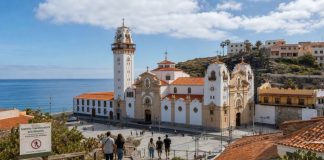 Afluencia en Candelaria: por qué hubo menos peregrinos Vista de la Basílica de Candelaria y su entorno costero con peregrinos descendiendo hacia la plaza y un aviso de restricción de sendero por riesgo de incendio.