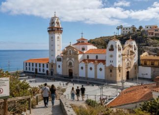 Afluencia en Candelaria: por qué hubo menos peregrinos Vista de la Basílica de Candelaria y su entorno costero con peregrinos descendiendo hacia la plaza y un aviso de restricción de sendero por riesgo de incendio.