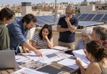 Placas solares en comunidad: de la junta a la instalación Vecinos reunidos en una azotea con placas fotovoltaicas mientras revisan planos y documentación de una instalación solar comunitaria.