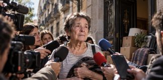 Culpa individual: la coartada para no hablar de vivienda Mujer mayor rodeada de cámaras y micrófonos frente a una vivienda, como símbolo de cómo un desahucio puede convertirse en juicio público sobre la persona.