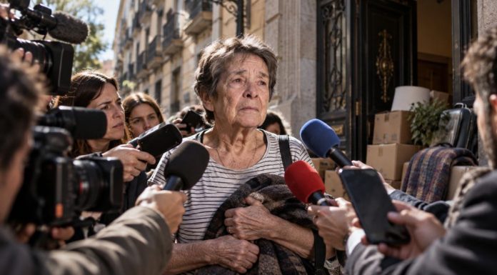 Culpa individual: la coartada para no hablar de vivienda Mujer mayor rodeada de cámaras y micrófonos frente a una vivienda, como símbolo de cómo un desahucio puede convertirse en juicio público sobre la persona.