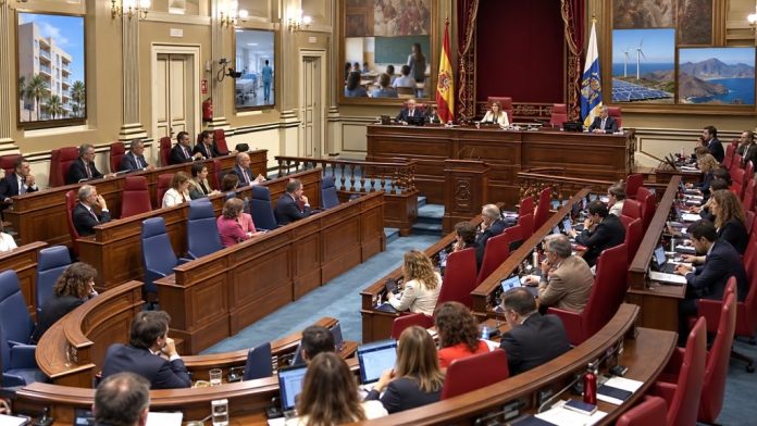 Salón de plenos del Parlamento de Canarias durante una sesión, con referencias visuales a vivienda, sanidad, educación, energía y territorio.