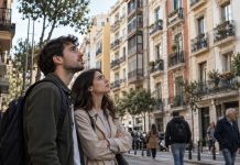 Barómetro de vivienda 2026: consensos y desigualdades Una pareja joven contempla los edificios de viviendas de una ciudad española, mientras personas de distintas generaciones transitan por la calle, reflejando la preocupación social por el acceso a la vivienda.