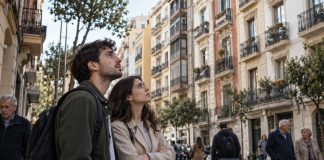 Barómetro de vivienda 2026: consensos y desigualdades Una pareja joven contempla los edificios de viviendas de una ciudad española, mientras personas de distintas generaciones transitan por la calle, reflejando la preocupación social por el acceso a la vivienda.