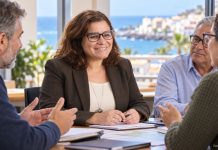 Mari Brito al Congreso: una voz municipalista para Canarias Mari Brito conversa con vecinos alrededor de una mesa, con un paisaje costero canario al fondo, en una escena recreada de diálogo municipal.