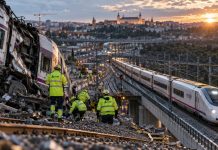 Ferrocarril español: inversión, seguridad y fiabilidad Recreación fotorrealista de un tren accidentado con operarios ferroviarios trabajando entre los restos, mientras un AVE circula por un viaducto cercano, reflejando los desafíos de seguridad y mantenimiento del ferrocarril español.
