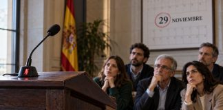 Pensiones y transparencia: Feijóo, Vox e Inda Cinco ciudadanos observan un atril vacío con el micrófono silenciado y un calendario que destaca el 29 de noviembre, como símbolo del silencio electoral.