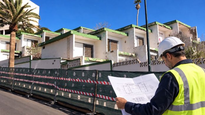 Ilustración fotorrealista de un ingeniero con casco y chaleco reflectante revisando planos de demolición frente al antiguo hotel Tenerife Tour, en Las Caletillas.